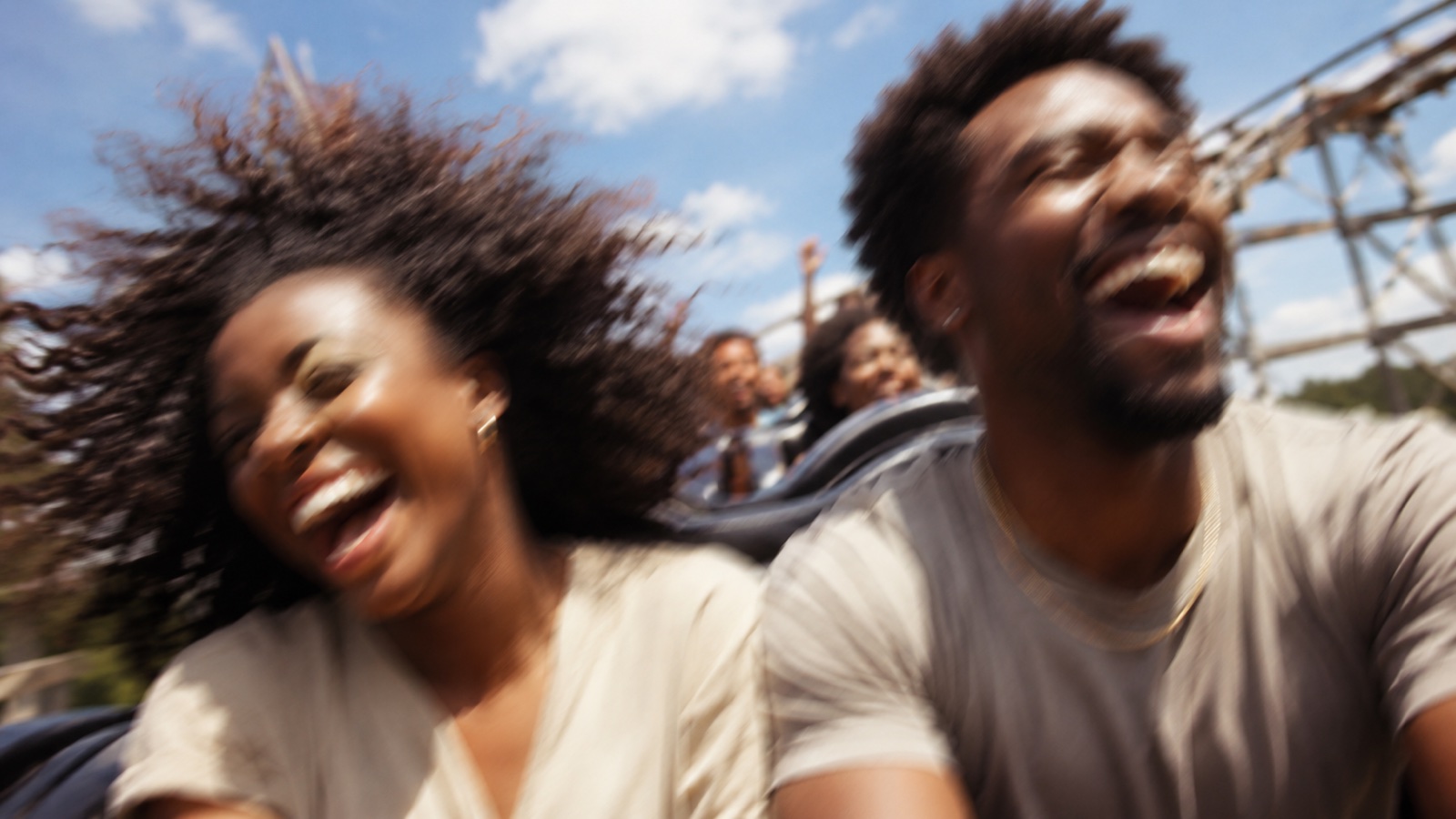 People laughing with arms raised on a rollercoaster